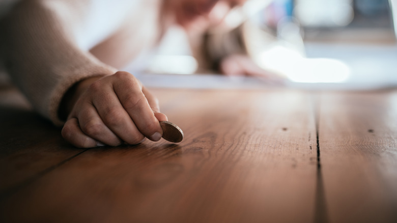 Person picking up a coin off a wooden floor underneath a couch