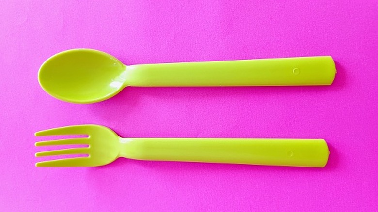 Green plastic utensils on a pink background