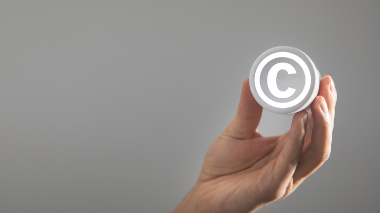 A hand holding the copyright logo over a gray background