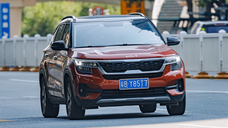 A Kia Seltos with an EU-style license plate driving down a city road