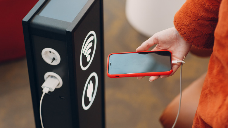 person charging an iPhone at a public charging dock