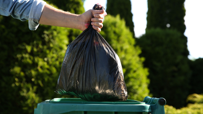 A hand holding a trash bag over a street garbage can