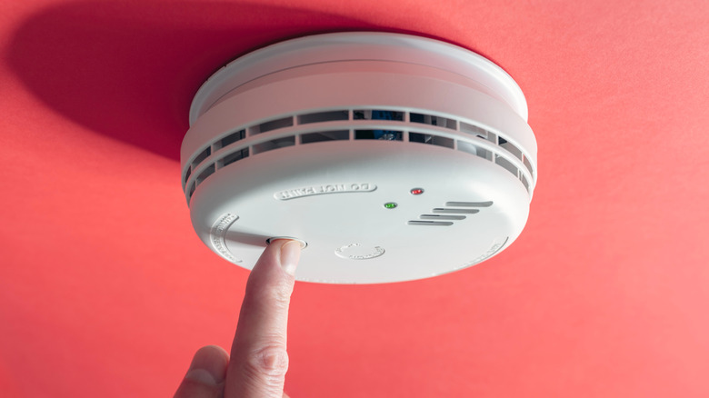 A finger pressing the button on a smoke alarm on the ceiling