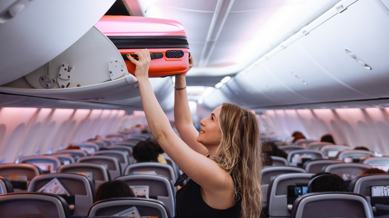 Woman putting carry-on into overhead bin