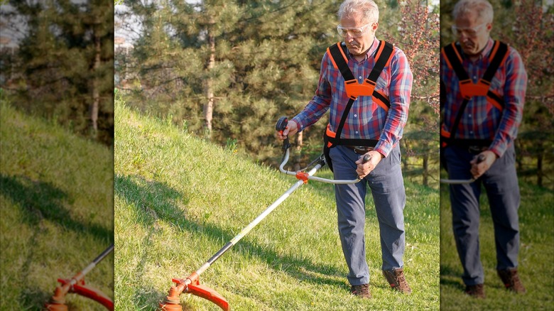 A person wearing a harness while trimming grass.