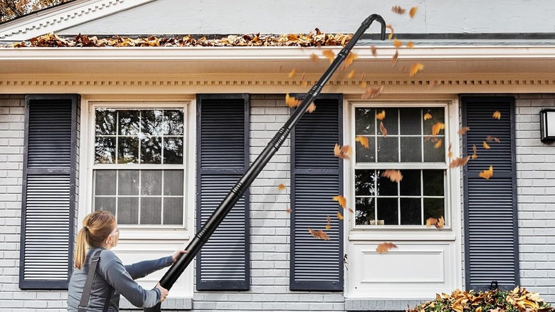 A person using a blower extension kit on gutters.