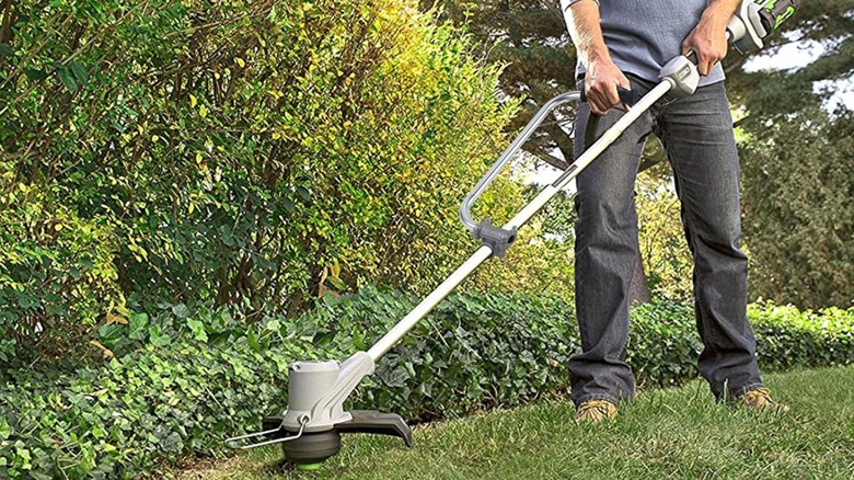 A person using a string trimmer with an additional handle.