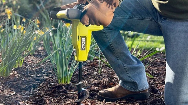 A person using a Ryobi auger on soil.