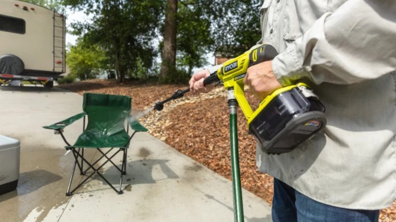 A person using a Ryobi power washer on a chair.