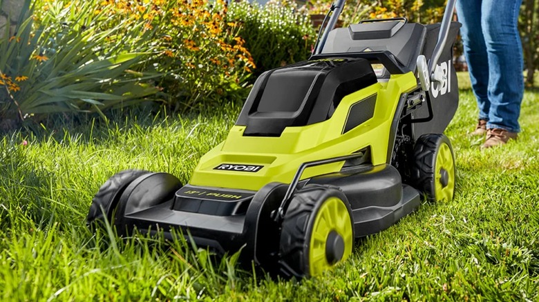 A person using a Ryobi lawn mower on grass.