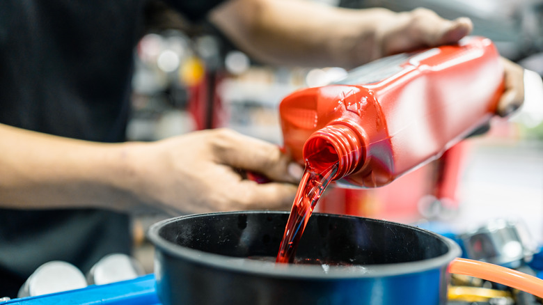 A person pouring bright red transmission fluid into a funnel
