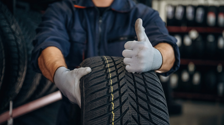 Mechanic holding a car tire gives a thumbs up.
