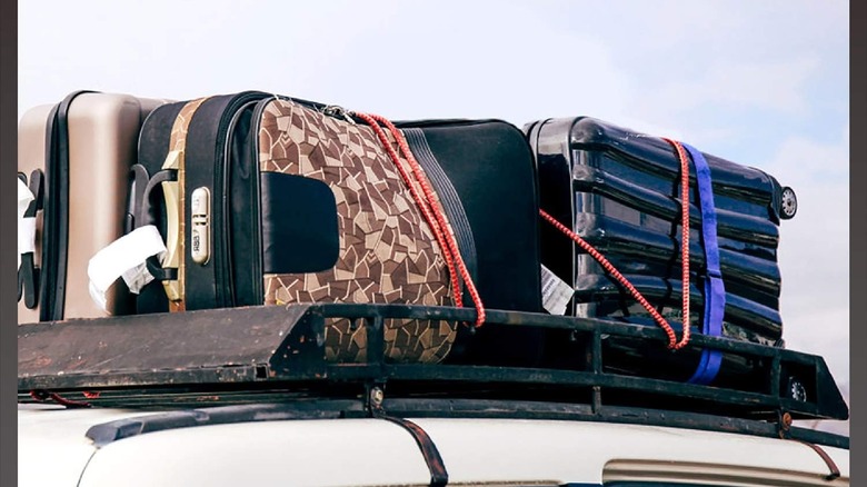 A bunch of suitcases tied to the top of a car.
