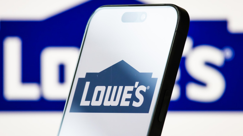 A Lowe's logo on a phone in front of a larger Lowe's logo.
