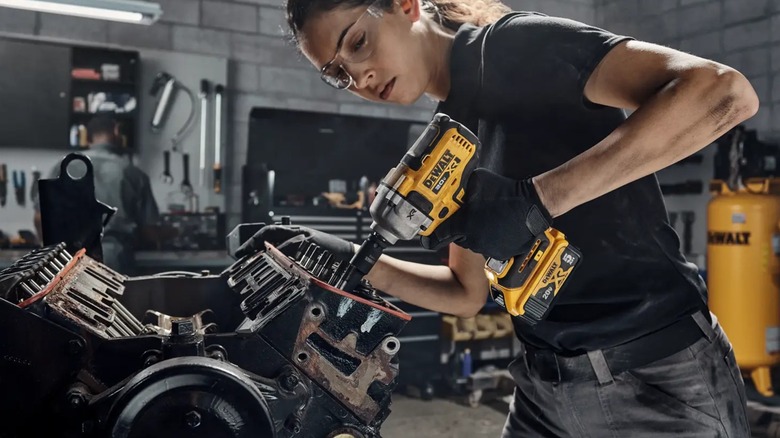 Person using a DeWalt impact drill on an engine.