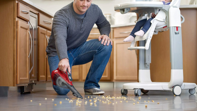 A man cleaning up cereal off of a kitchen floor with a Black and Decker vacuum