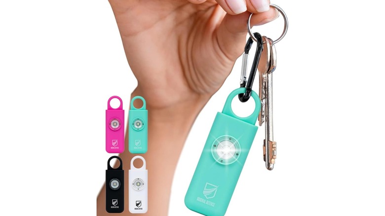 Hand holding a teal keychain alarm on a key ring