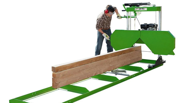 Man operating green portable saw mill against white background