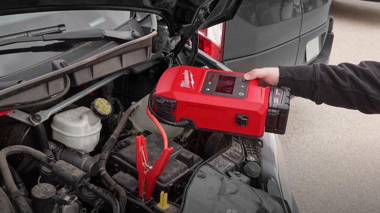 Hand holding Milwaukee jump starter while jump starting car