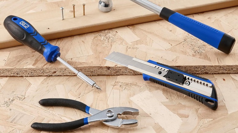 Screwdriver, plier, blade, and hammer on wood pieces