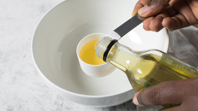 A person using the flour measuring cup to measure oil