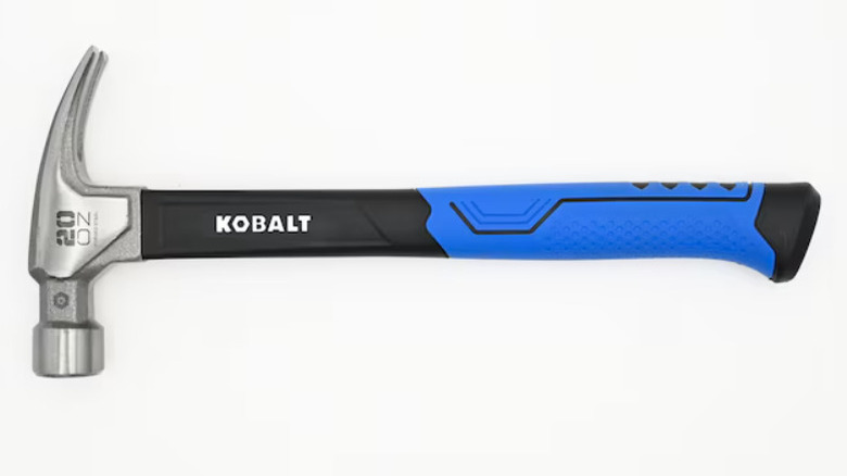Kobalt hammer about to hit a nail into a piece of board held by someone with a wooden wall background