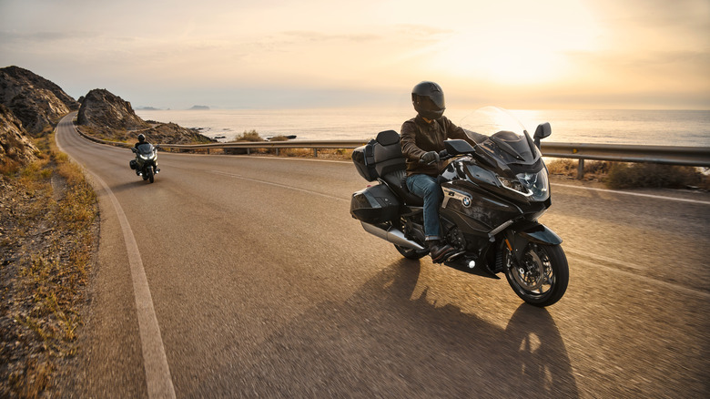 Two riders moving down a coastal road, each on a current-generation BMW K1600 GT from 2022 or later in the late afternoon.
