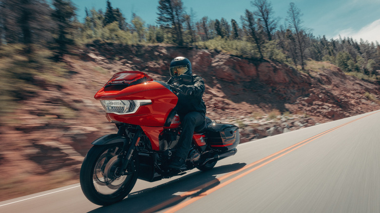 A reddish orange 2026 Harley-Davidson CVO Road Glide ST being ridden at speed by a rider in full gear.