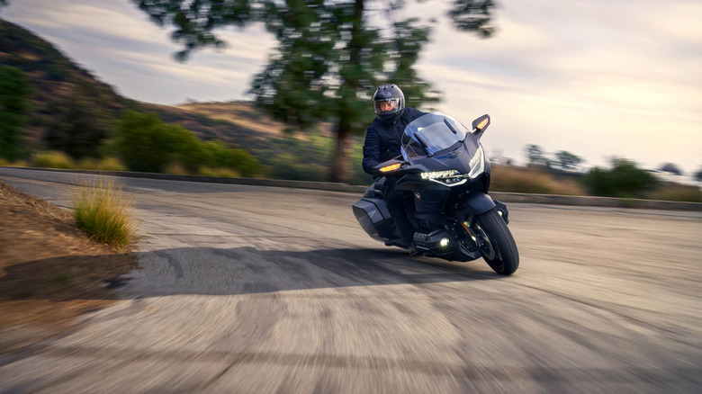 A rider in a full-face helmet and gear taking a turn at speed on a 2025 Honda Gold Wing touring motorcycle.