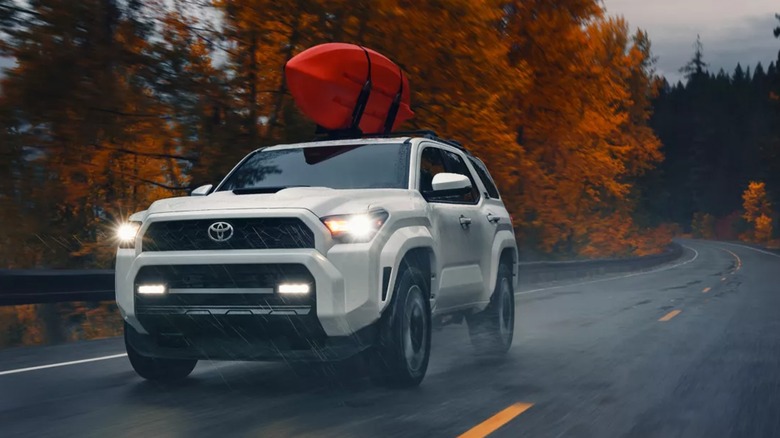 A white Toyota 4Runner with a kayak on its roof, traveling down a wet autumn road