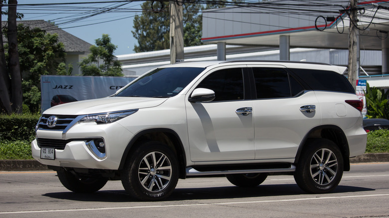 Side view of white Toyota Fortuner driving on street in Thailand.