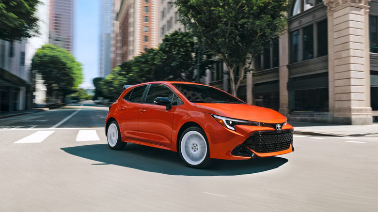 A 2026 Toyota Corolla hatchback, finished here in the "Inferno" colorway, moving through a downtown city area.