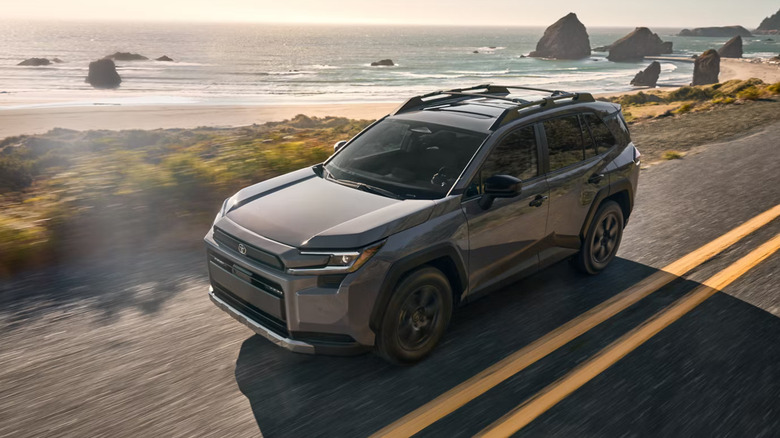 A 2026 Toyota RAV4 finished in dark gray moving at speed along a coastal road with double yellow lines visible on the road.