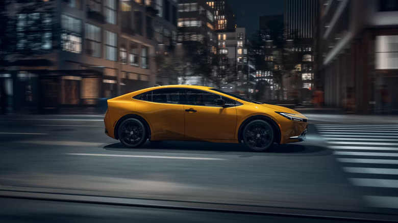 A 2026 Prius from Toyota, in the "Karashi" yellow paint scheme, moving at speed at night down a city street.