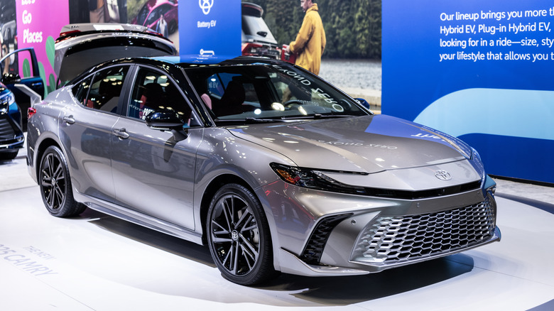 A front-three-quarters view of the 2026 Toyota Camry finished in dark gray at an indoor exhibition.
