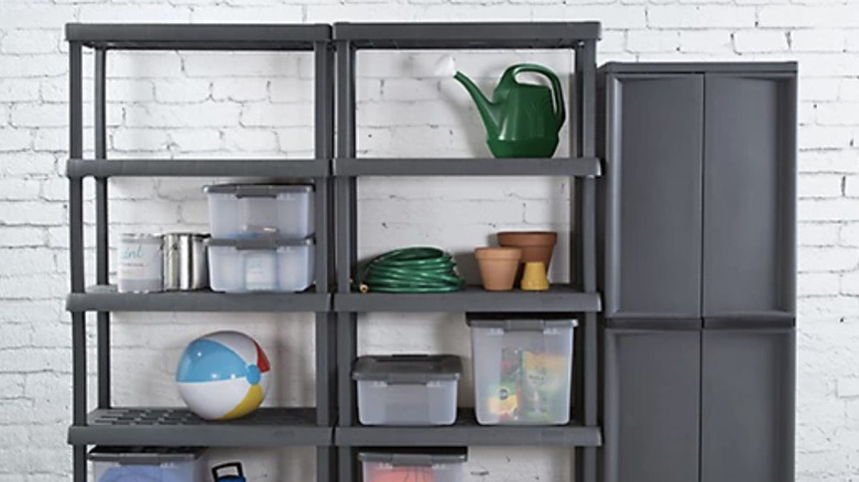 Two Sterilite plastic shelvings units sitting with a tall, closed plastic cabinet against a white brick wall