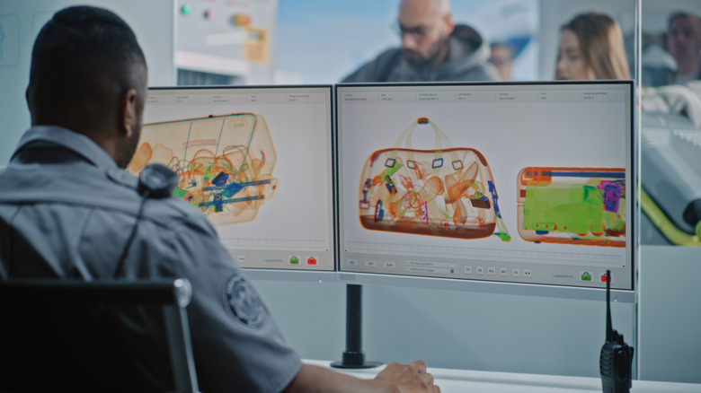 Airport security officer views the contents of bags on two screens.