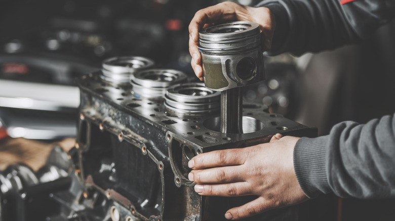 A mechanic handling a four-cylinder engine block.