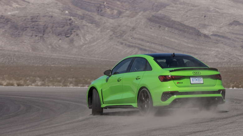 Rear view of green Audi RS 3 drifting on desert race track.