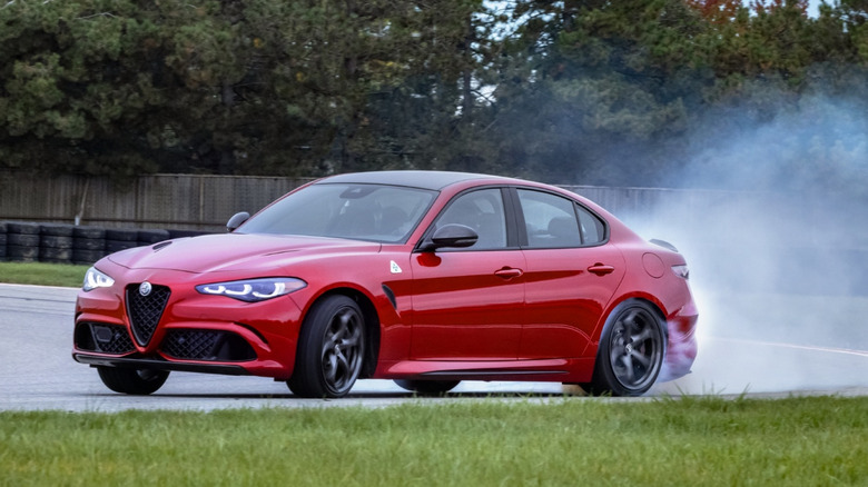 Front 3/4 view of red Alfa Romeo Giulia Quadrifoglio drifting on race track.