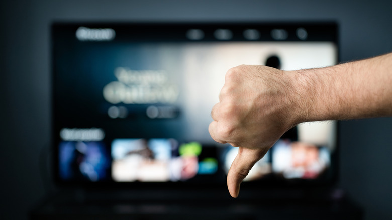 Blurred television with an in-focus hand in front doing the "thumbs down" gesture