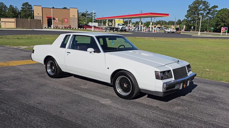 A gorgeous white Buick Regal T-Type from 1987 standing at the side of a wide asphalt road on a sunny day.