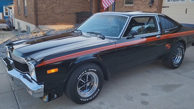 A black Dodge Aspen R/T miscle coupe with racing stipes, parked on a pavement, front left view visible.