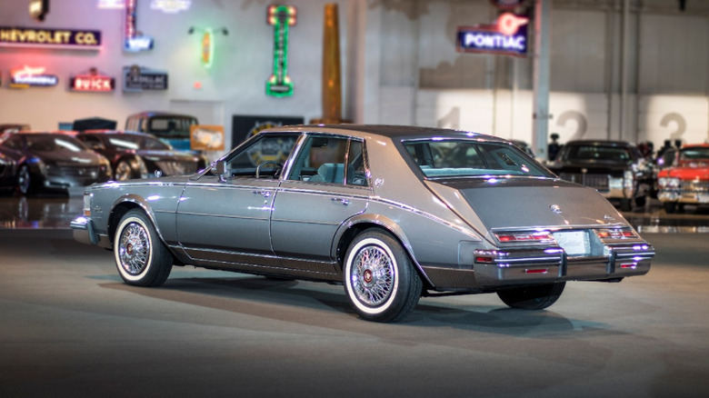 A back-left view of a blue first-generation Cadillac Seville parked inside a warehouse-like garage.