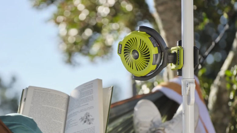 Person reading book with Ryobi misting fan attached to pole nearby