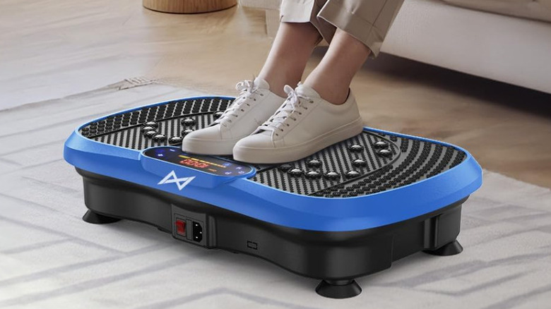 A person, their feet in sneakers, on a vibration plate on living room floor