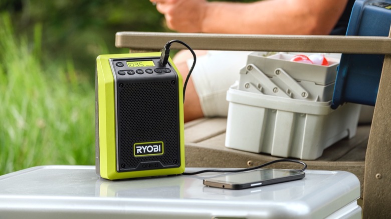 A Ryobi Bluetooth speaker with smartphone connected, in a green field