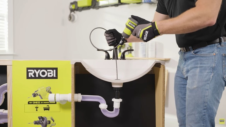 Ryobi USB Lithium auger being demonstrated with the drain cable inserted in a drain hole.