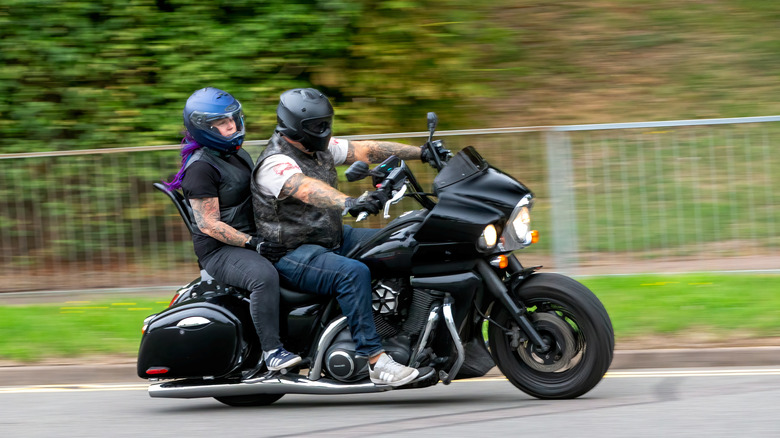 A 2011 Kawasaki Vulcan VN finished in black traveling down a road with two riders wearing helmets on it.