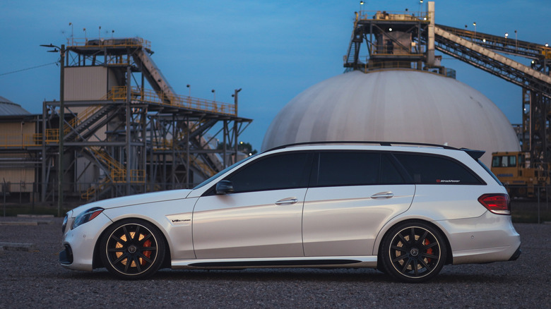 Side view of white Mercedes E63 AMG wagon parked in industrial area.